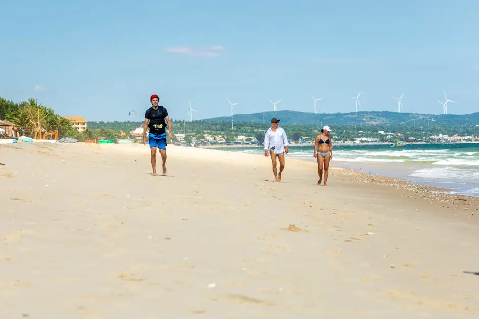 Three people walking along a sunny beach with wind turbines in the background, showcasing a mix of leisure and sustainability.