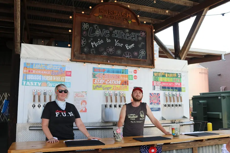 Two bartenders at a craft beer stand ready to serve unique beverages on a sunny day.