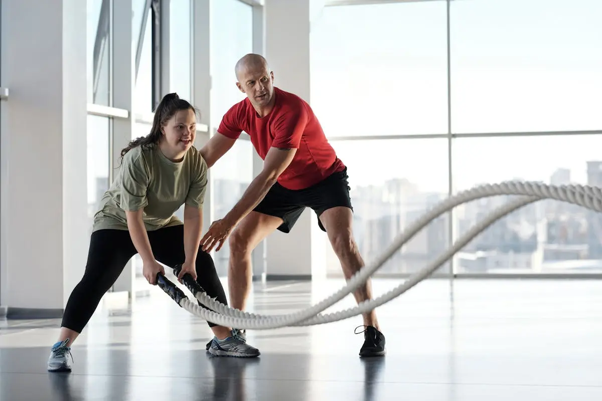 Woman and trainer engaging in rope workout in a bright gym, showcasing inclusivity and fitness motivation.
