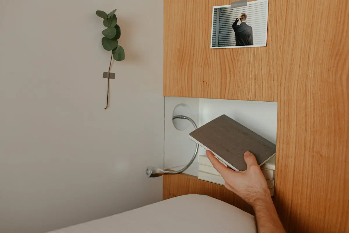 Hand placing a book on a sleek wooden shelf with decorative elements.