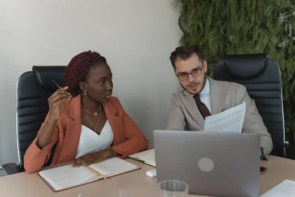 Two diverse professionals engage in a meeting, discussing documents and ideas in a modern office environment.