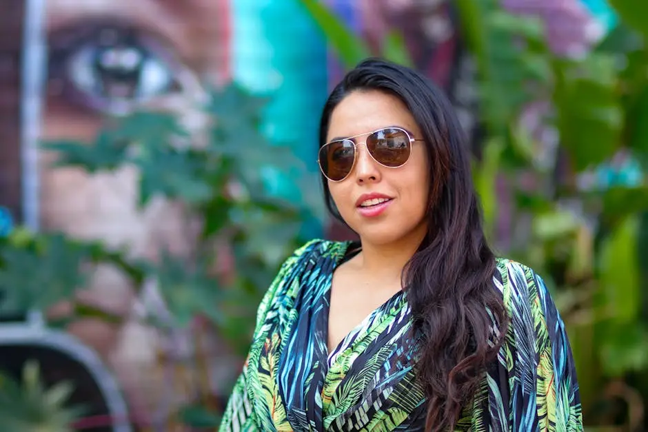 Confident woman in sunglasses posing outdoors in vibrant Ciudad de México with artistic mural background.