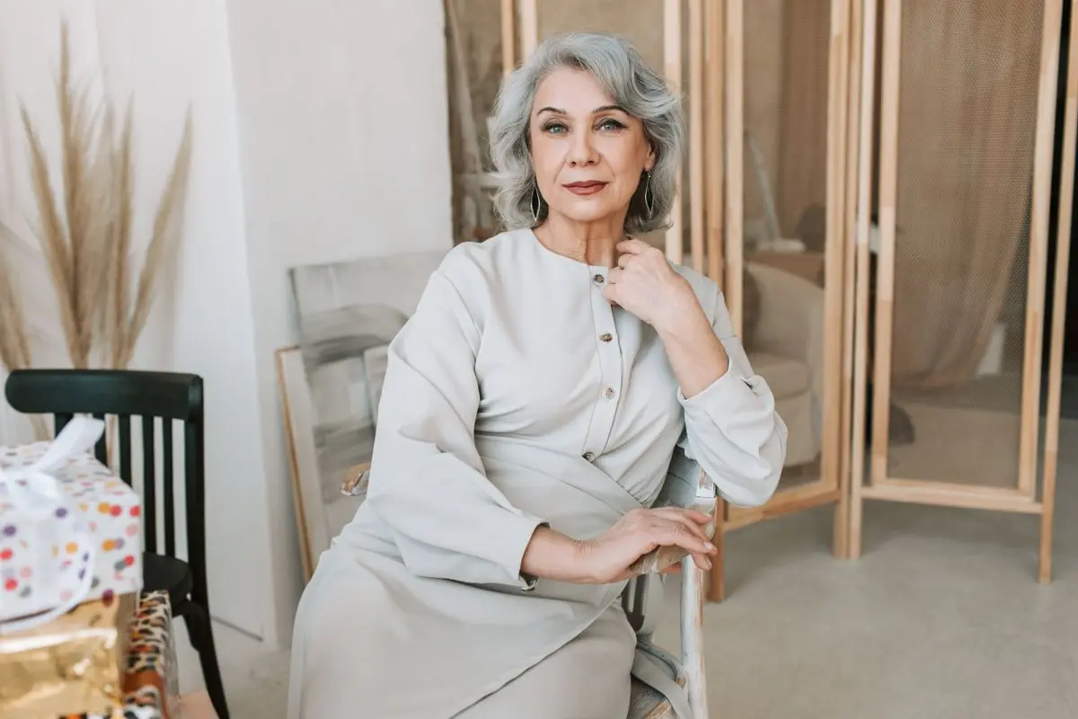 Sophisticated senior woman with silver hair poses gracefully indoors, exuding elegance.