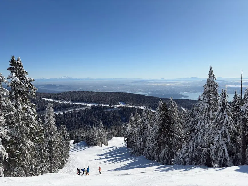 Snow-covered trees and skiers on a scenic slope in West Vancouver, BC, on a clear winter day.