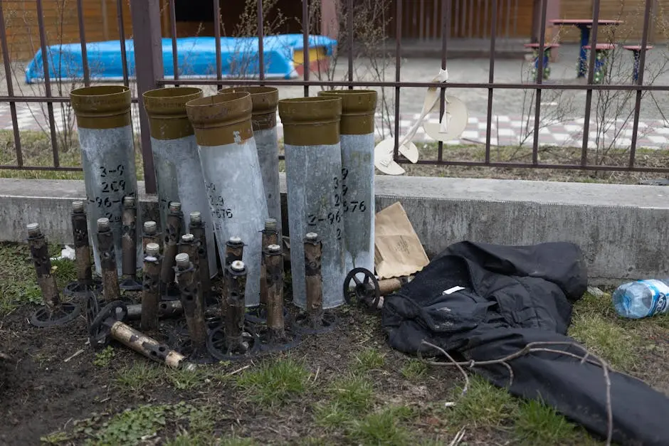 Outdoor scene showing discarded industrial equipment and miscellaneous litter beside a fence.