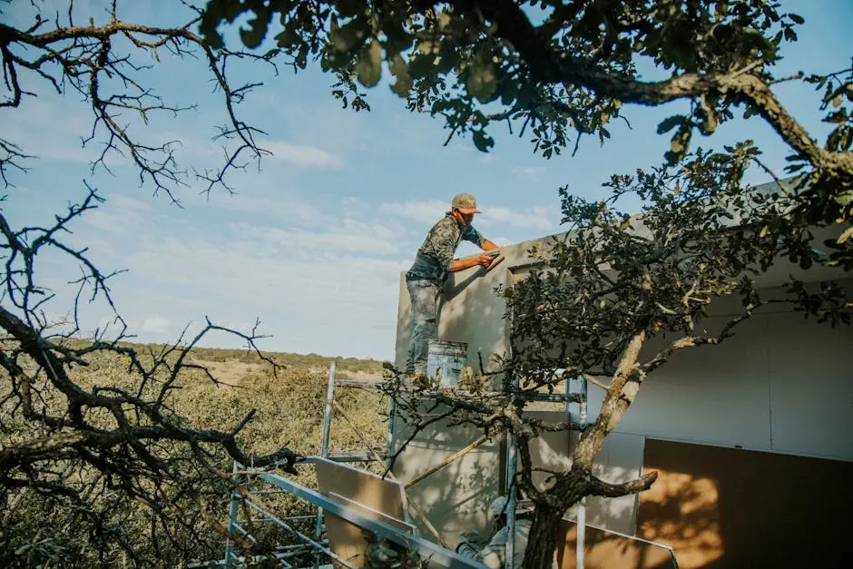 A construction worker repairs a roof surrounded by trees, showcasing outdoor craftsmanship.