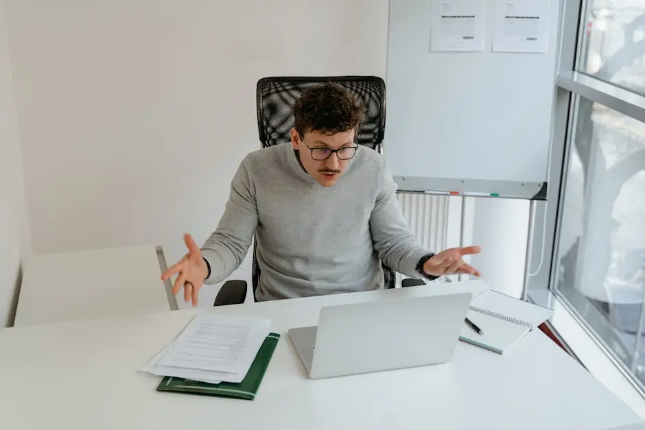 A businessman in a gray sweater expressing frustration during a virtual office meeting.