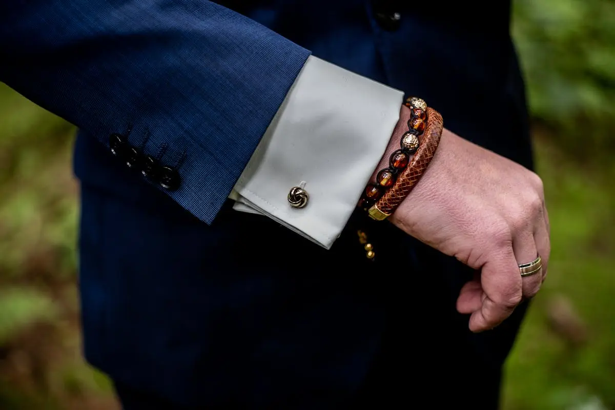 A stylish close-up of a man’s hand showing a suit sleeve, bracelet, and ring.