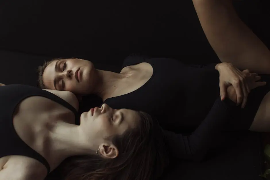 Two women lying down in black bodysuits with eyes closed, creating a serene and artistic composition.