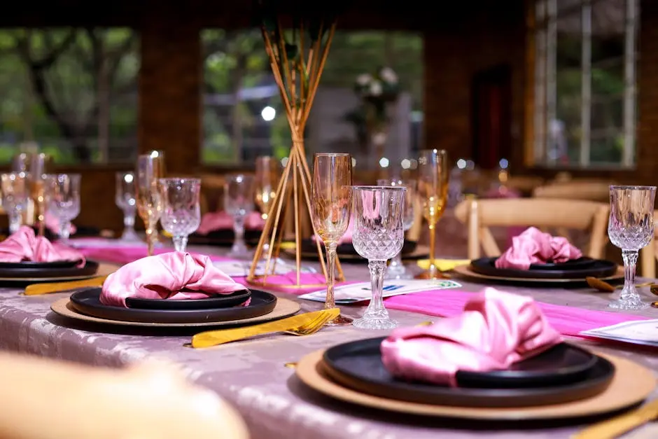 A beautifully arranged dining table with pink napkins, crystal glasses, and gold cutlery, perfect for elegant events.