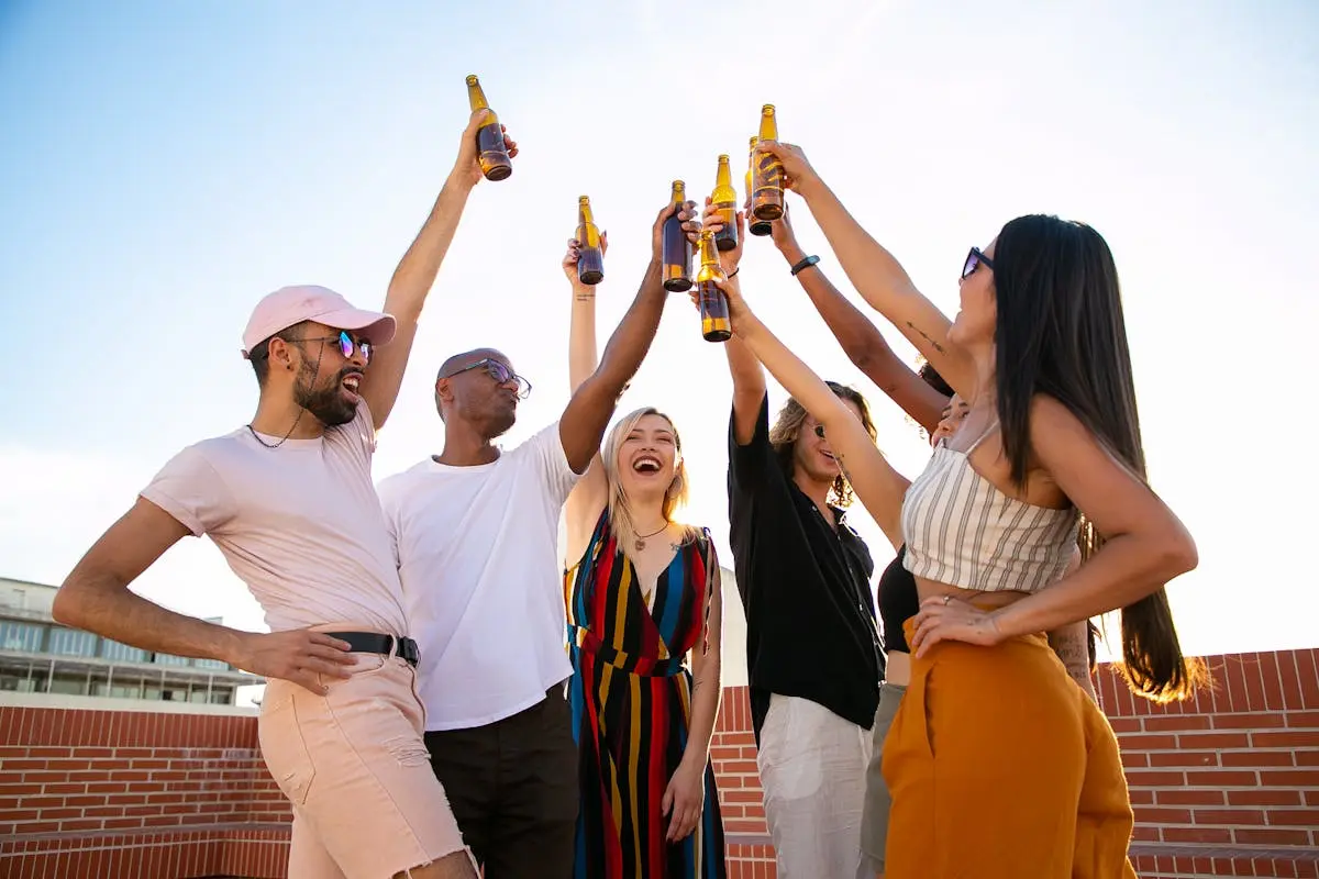 Group of diverse friends enjoying drinks and laughter on a sunny rooftop.