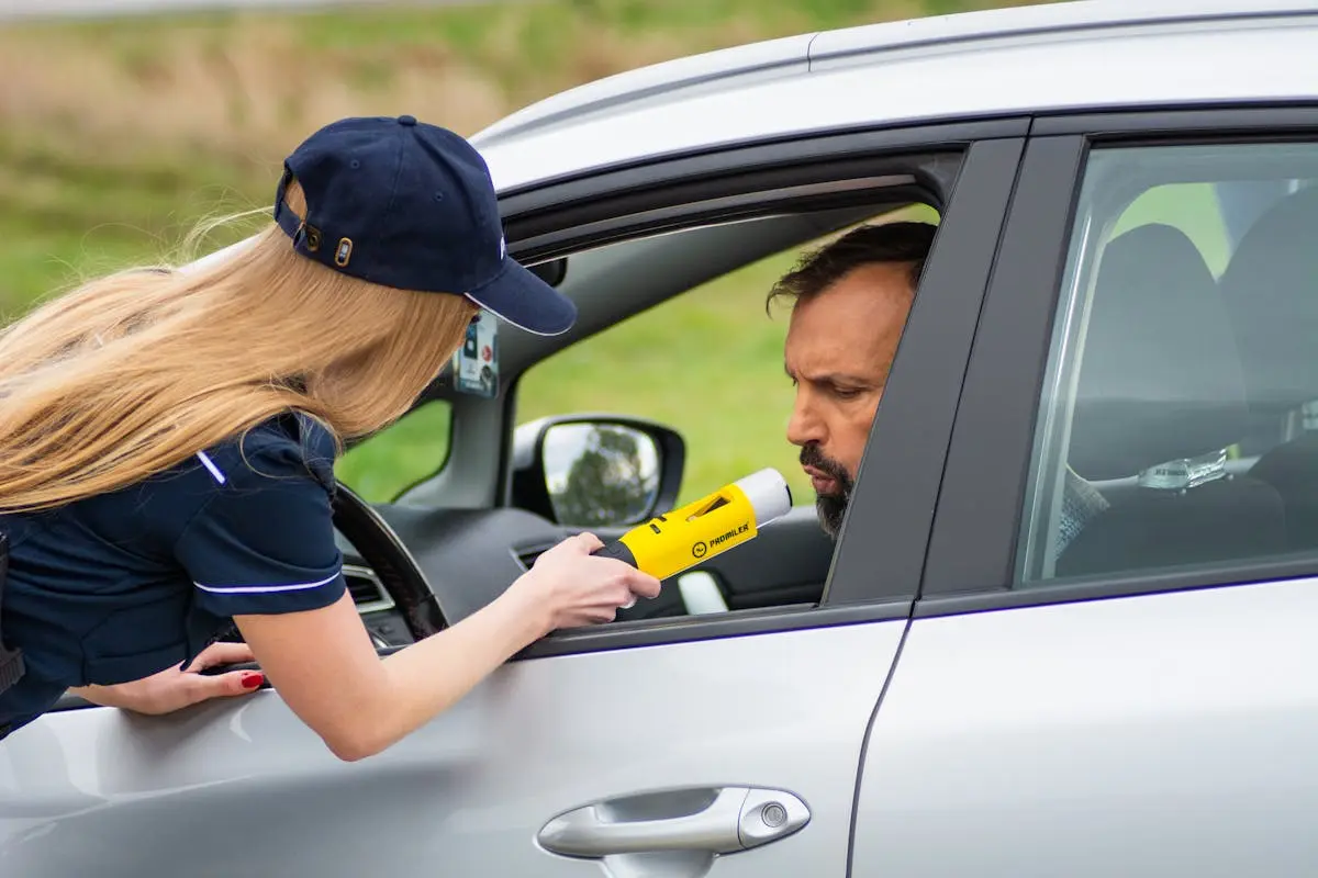 Police officer using breathalyzer to test driver's alcohol level outside car.