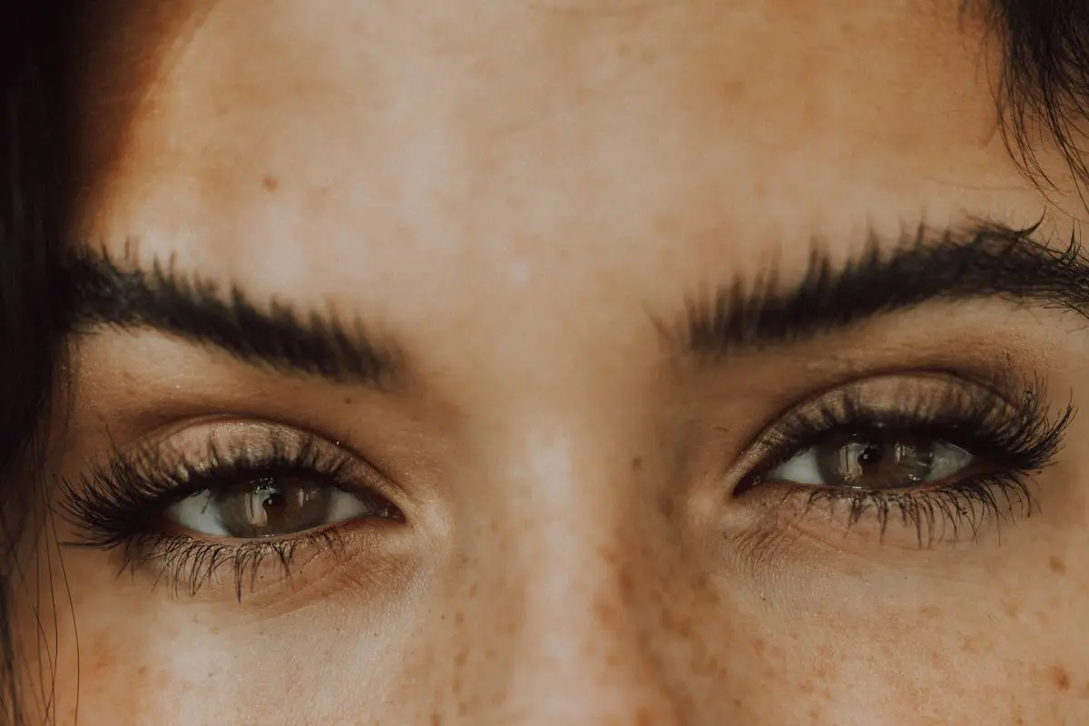 Detailed close-up photo capturing freckled eyes and thick eyebrows of a person, emphasizing natural beauty.
