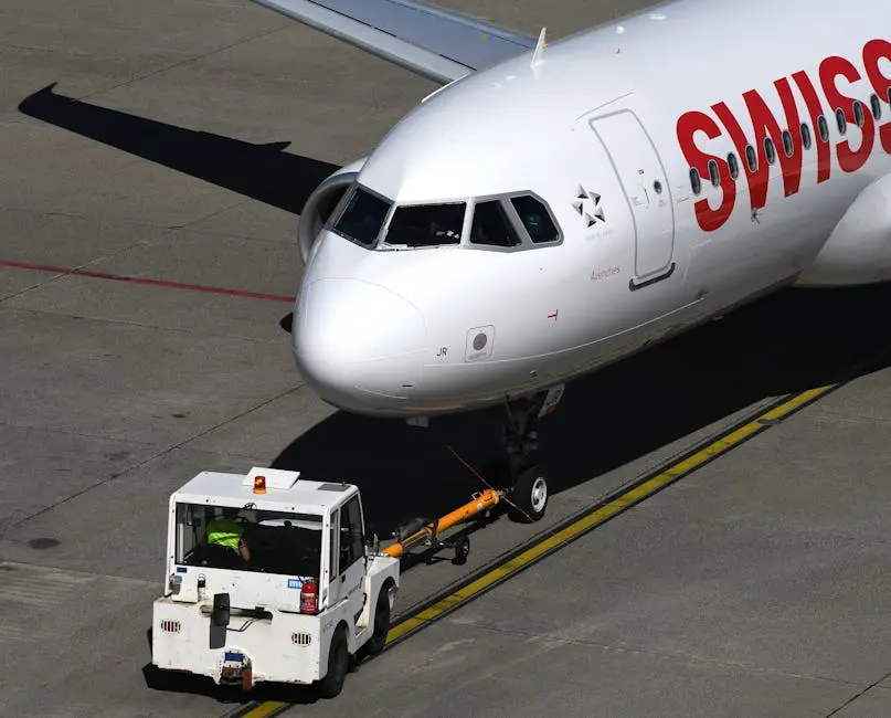A Swiss aircraft being towed by a vehicle at Geneva Airport captured from above.