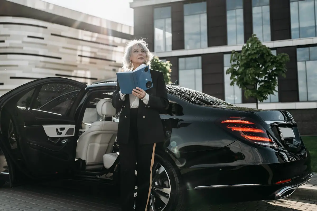 Senior businesswoman exits a black luxury car, holding documents near modern office building.