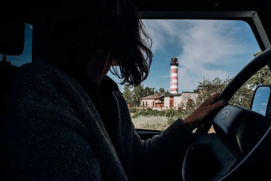 A woman driving with a view of a striped lighthouse through the car window.