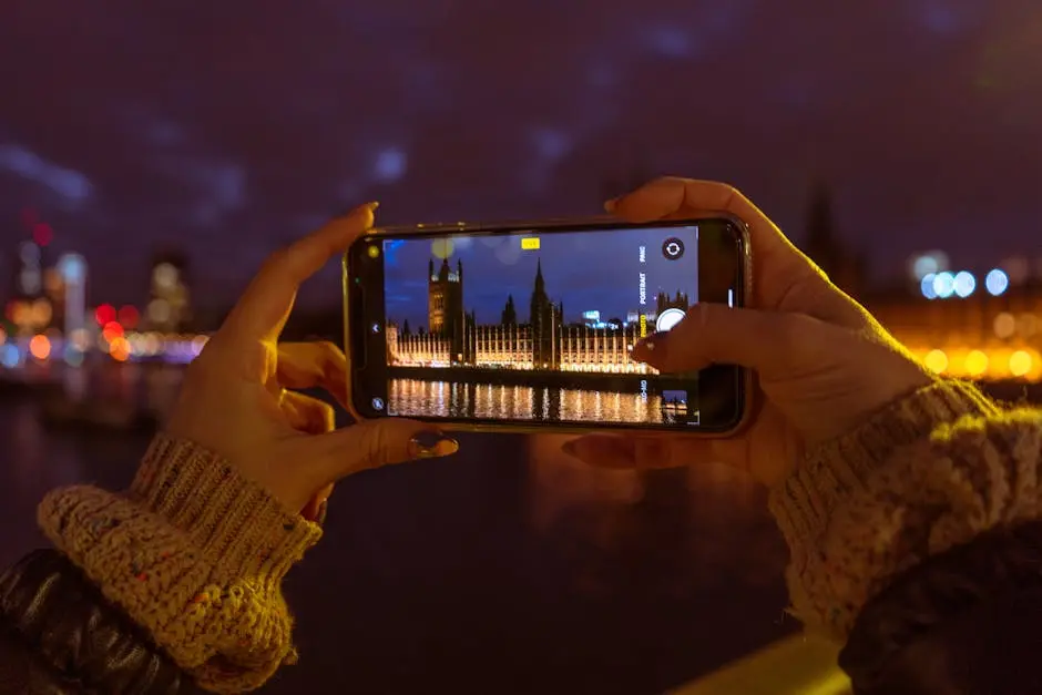 A person photographing London’s iconic skyline at night using a smartphone.