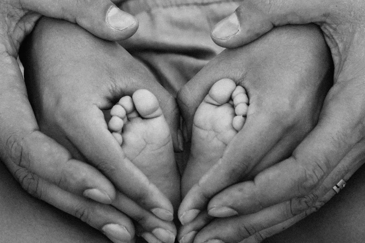 Black and white photo of adult hands cradling baby feet, symbolizing family love and connection.