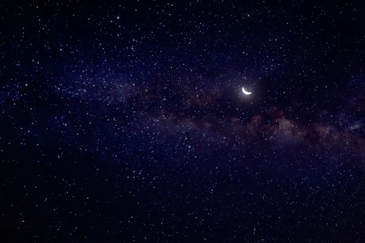 A breathtaking view of the starry night sky featuring the Milky Way and a waning crescent moon.