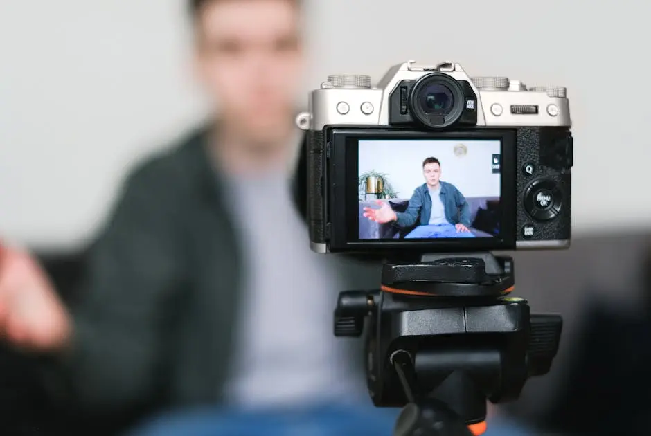 Man recording a vlog indoors using a mirrorless camera on a tripod with selective focus.