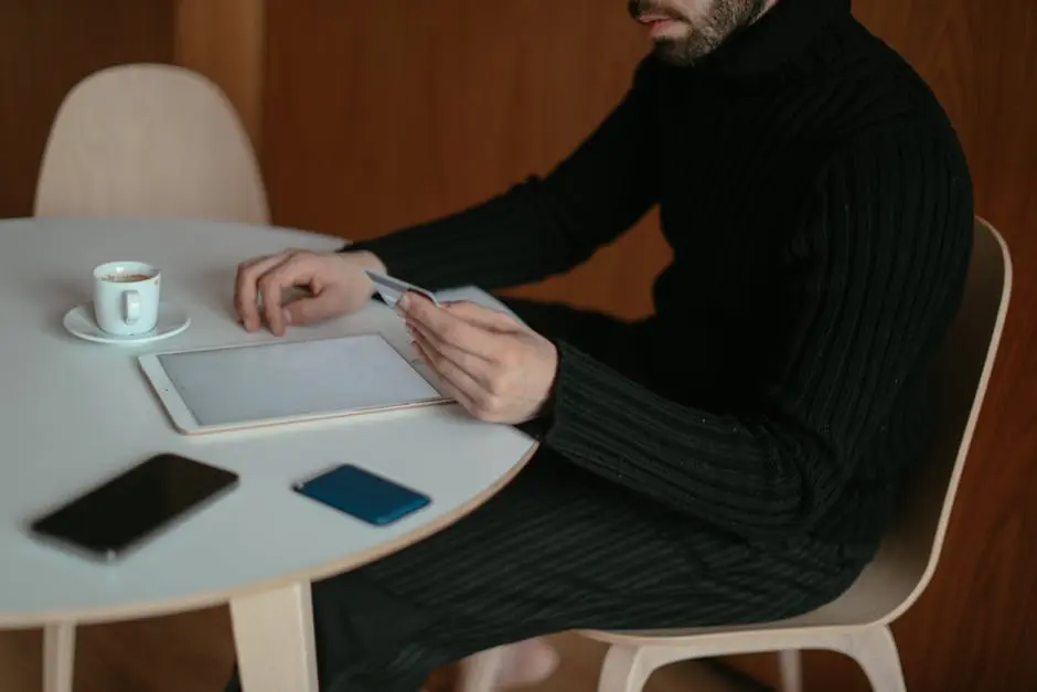 Adult man using tablet and credit card to shop online at home, sitting by table with coffee.