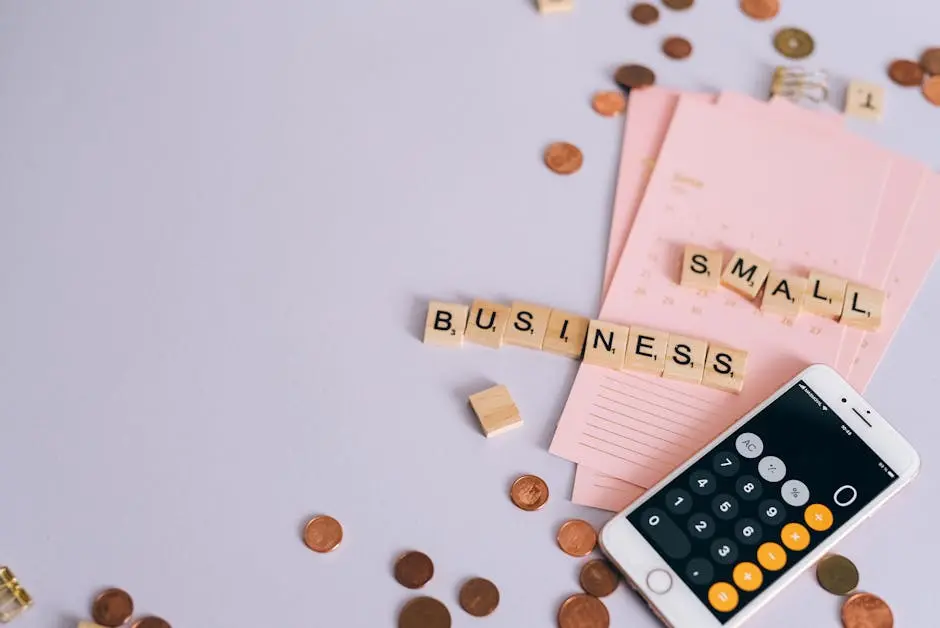 Flat lay of a small business planning scene with coins, smartphone calculator, and letter tiles.