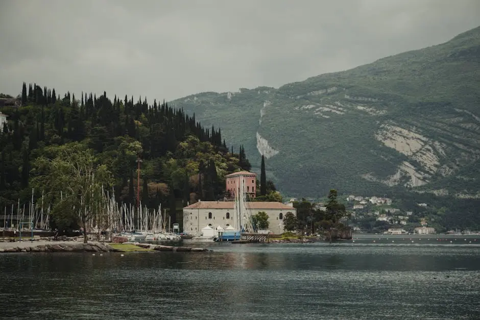 Picturesque view of a historic building by the water with lush greenery and sailboats.