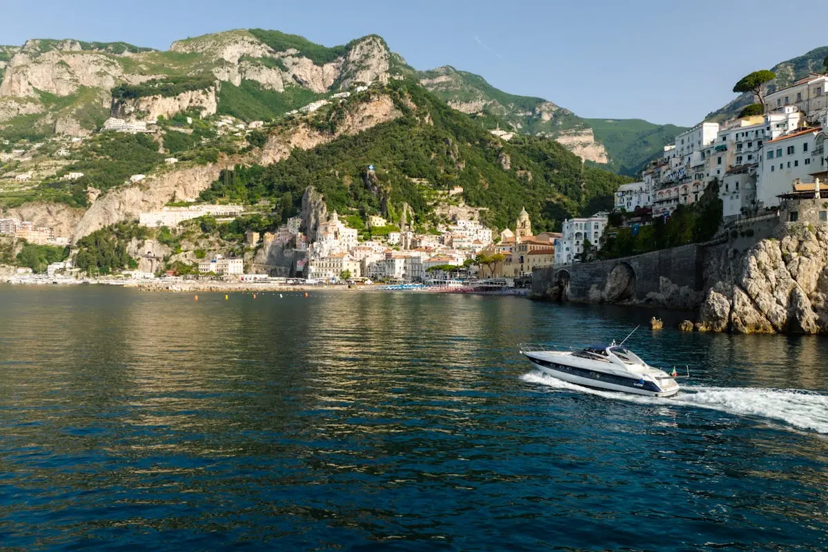 A yacht cruises along the picturesque Amalfi coastline under clear blue skies during summer.