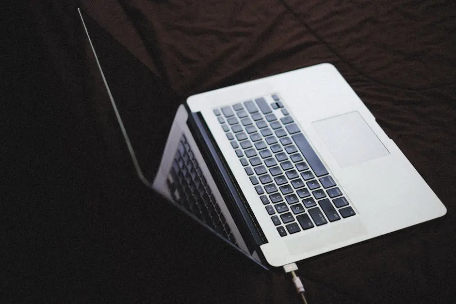 Modern laptop with backlit keyboard on a dark fabric surface, connected to a charger.
