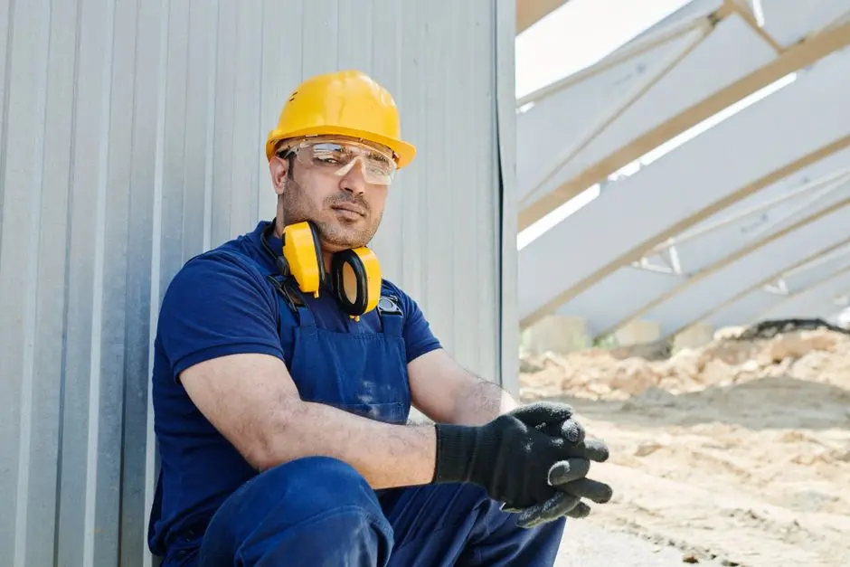 A male construction worker wearing safety gear sits at a construction site, showcasing standard industry protection.