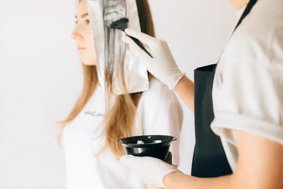 Hairdresser applying color to woman’s hair in salon using brush and foil technique.