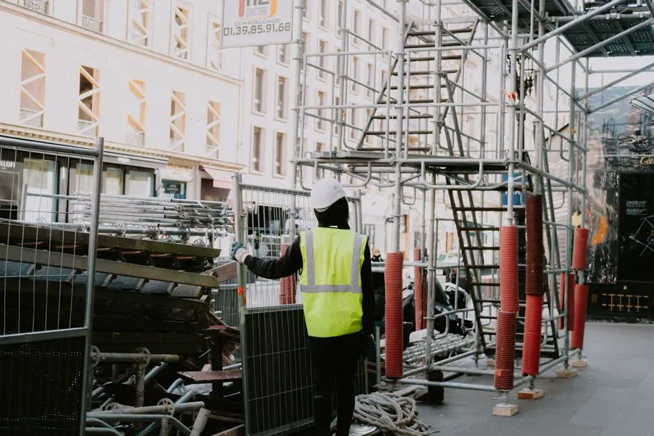 A construction worker onsite in a city wearing safety gear and examining scaffolding.