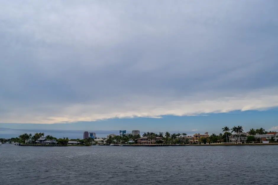 A tranquil coastal scene with tropical waterfront houses and palm trees under a cloudy sky.