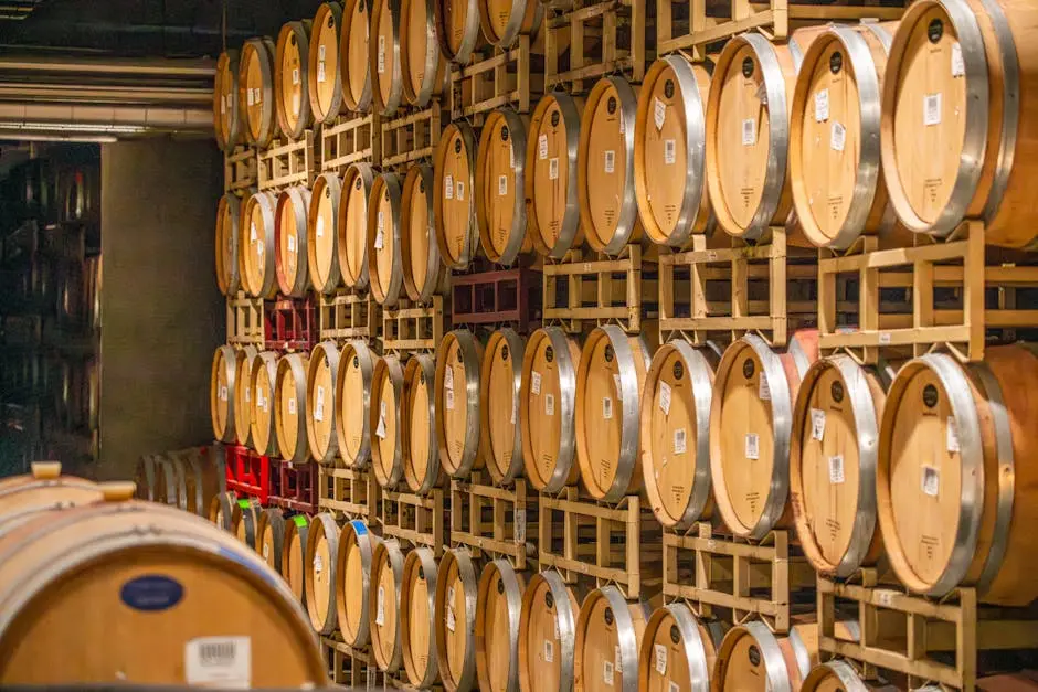 Rows of wooden wine barrels stacked in an indoor winery cellar, showcasing traditional aging process.