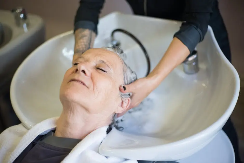 Senior woman relaxing during a hair wash at a salon. The hairstylist gently massages her hair in an inviting, serene setting.