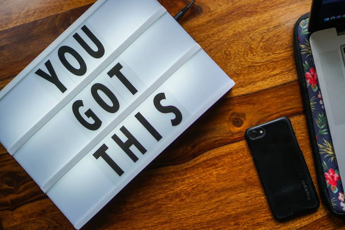 Motivational quote ‘You Got This’ on a lightbox, smartphone on a wooden table, cozy workspace vibe.