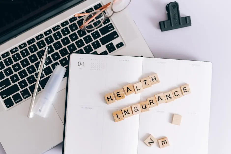Scrabble tiles spelling health insurance on a planner next to a laptop.