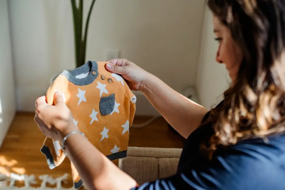 Side view of crop happy female choosing clothes for newborn baby while sitting on sofa at home