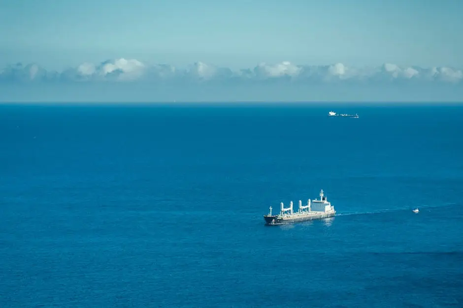 Wide aerial shot of a cargo ship sailing across the vast ocean under a clear sky.