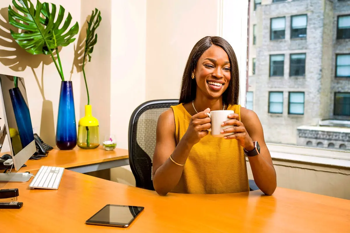 Confident woman in office attire enjoying a coffee break, showcasing modern workspace vibes.