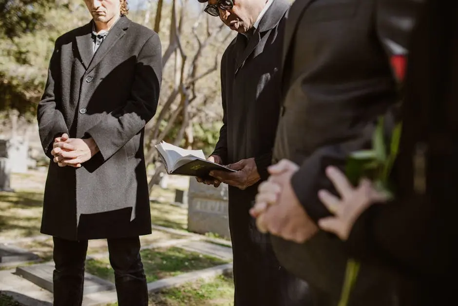 A group of people in black coats engage in thoughtful prayer at a cemetery service.