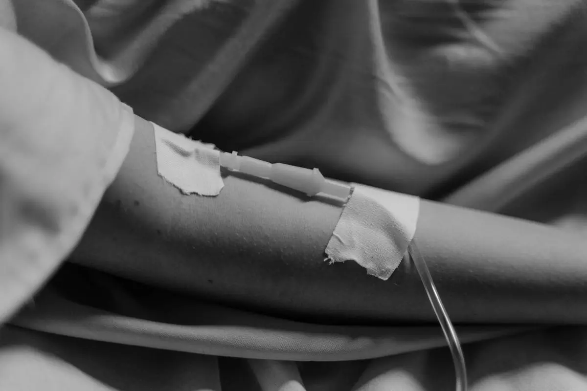 Monochrome close-up of an IV drip inserted in a patient’s arm, symbolizing medical care.