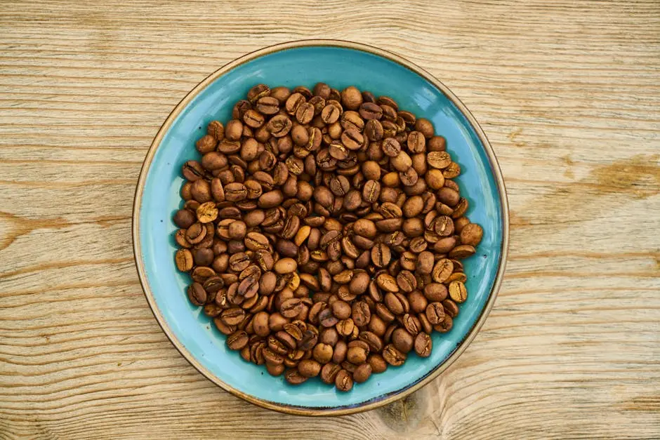 Top view of roasted coffee beans in a ceramic bowl on a wooden surface, perfect for coffee lovers.