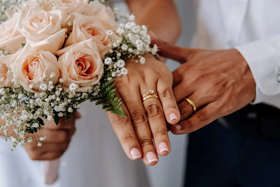 Close-up of wedding rings on couple’s hands with rose bouquet, symbolizing love and commitment.