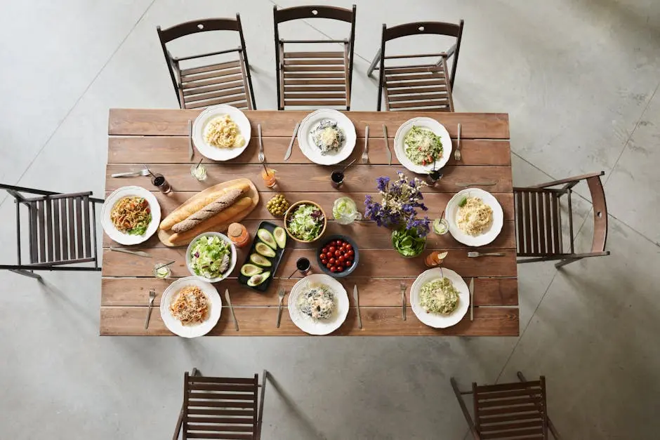 Top view of a wooden table set with pasta dishes, fresh ingredients, and drinks for a cozy meal.