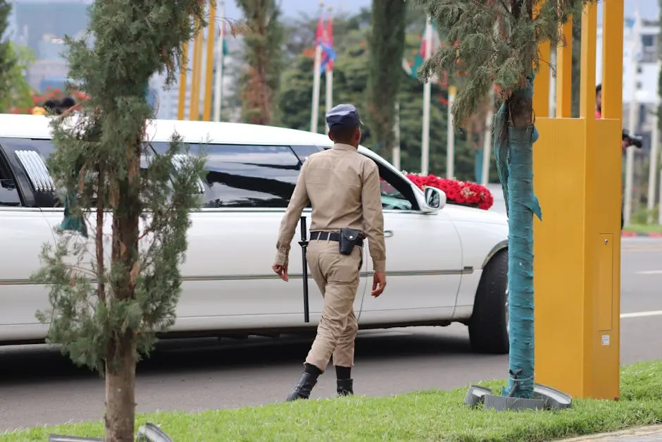 A security guard in uniform walking beside a white limousine outdoors.