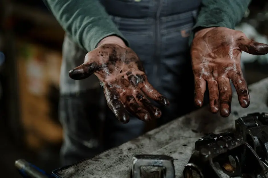 Close-up of a mechanic’s dirty hands in a garage workspace with grease and spare parts.