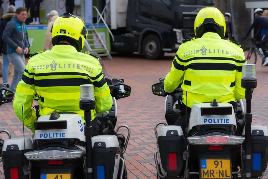 Two Dutch police officers in bright uniforms patrolling a public event on motorcycles.