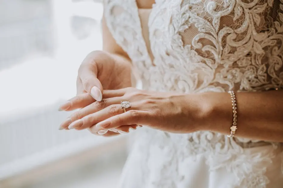 Close-up of a bride adjusting her wedding ring, showcasing elegant jewelry and embroidery.