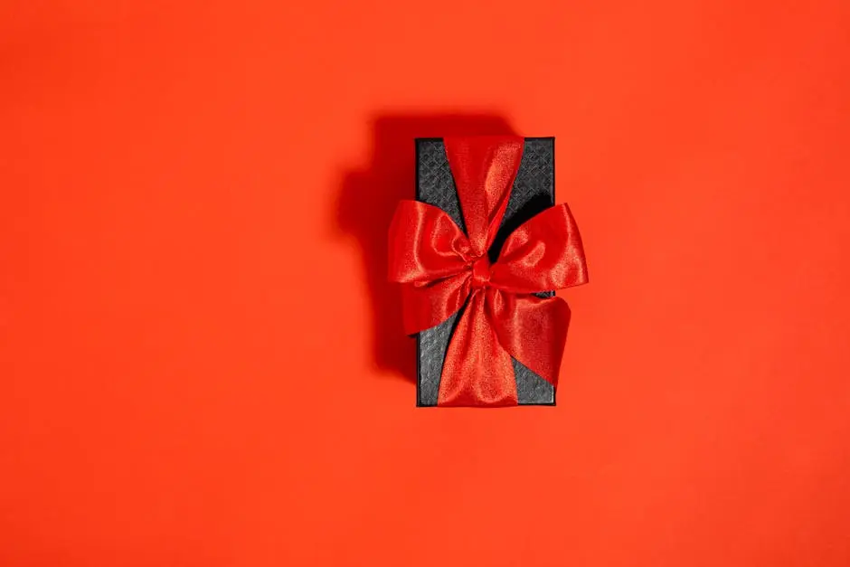 A stylish black gift box adorned with a luxurious red ribbon sits elegantly against a vivid red background.